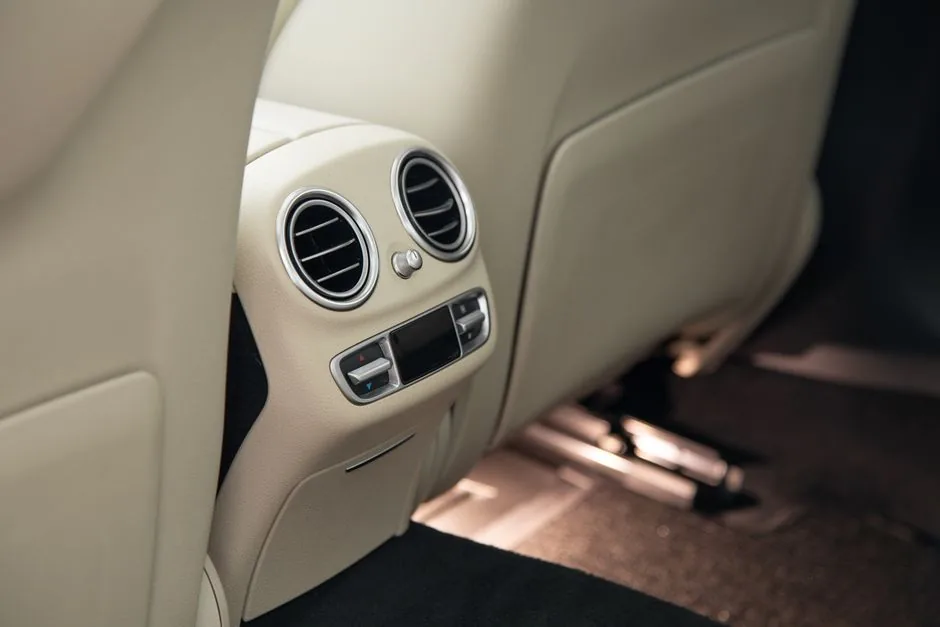 Rear car air conditioner vents blowing cold air onto a beige leather interior